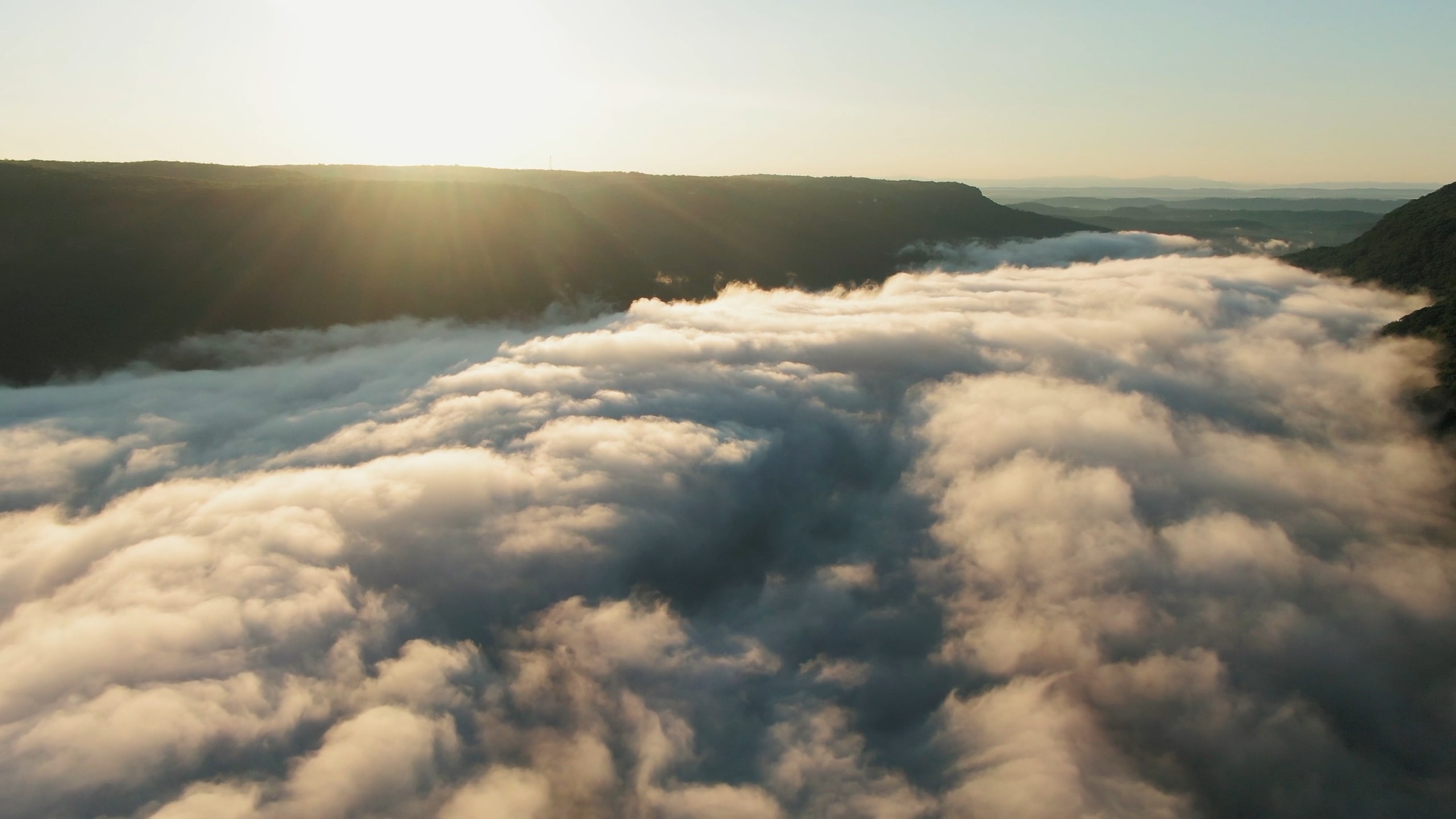 A drone image of rolling clouds over a Japanese landscape with a sunrise in the background